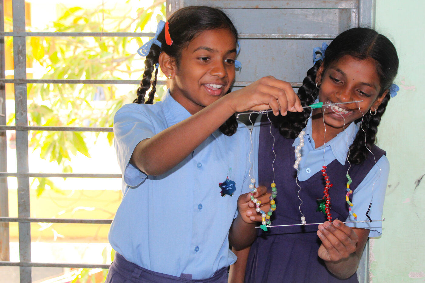 Two girls in school uniform examining and holding up their work near a window.