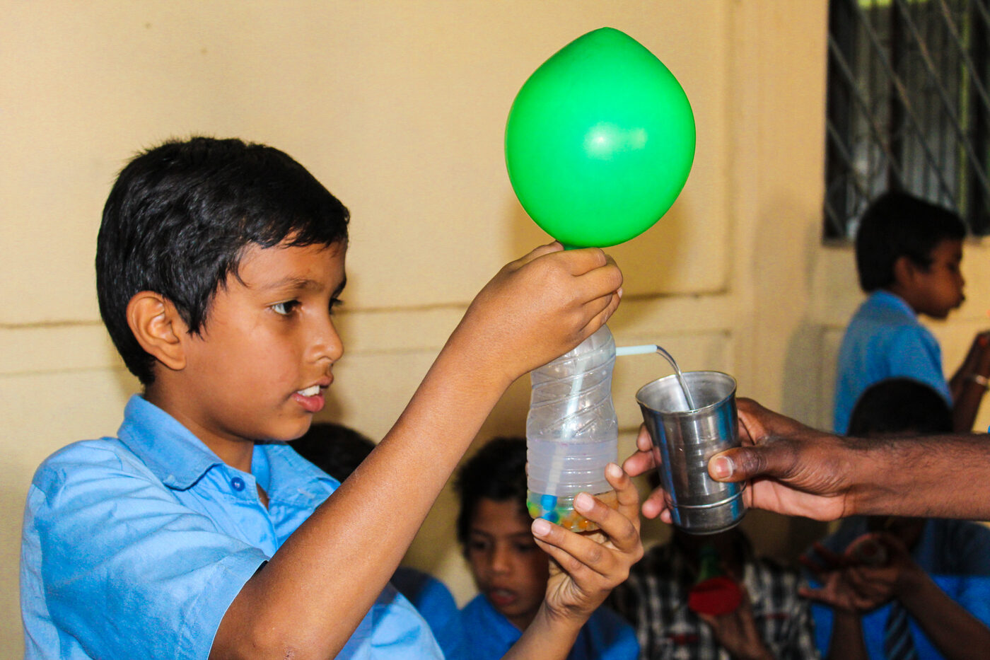 A boy in school uniform focused on a balloon-over-bottle air-pressure experiment.