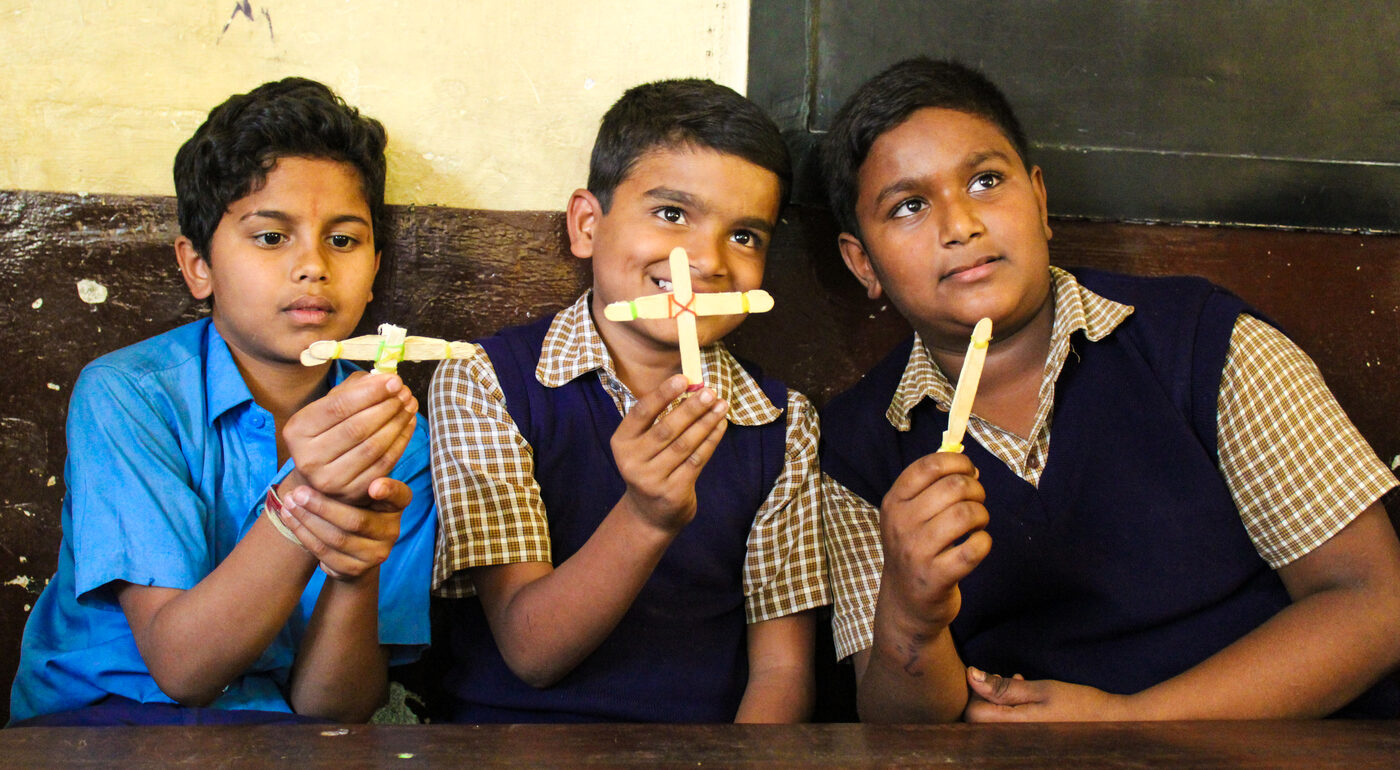 Students smiling proudly as they hold up the models they built in class.